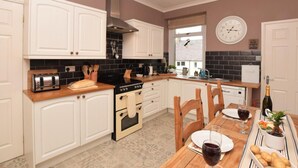 A kitchen with white cabinets, a stove, and a dining table set for two with plates and wine glasses. - 3 Bed in Morpeth (oc-cn137) (Amble)