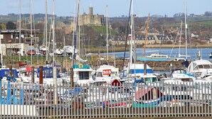A marina with numerous boats docked, a castle in the background, and a sign for Coquet Yacht Club. - 3 Bed in Morpeth (oc-cn137) (Amble)