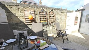 An outdoor dining area with stone walls, a round table, chairs, and a wine glass. - 3 Bed in Morpeth (oc-cn137) (Amble)