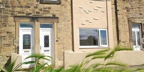 A building facade with two doors labeled 'PANHAVEN' and 'LITTLE PANHAVEN,' a stone wall, and a window with blinds. - 3 Bed in Morpeth (oc-cn137) (Amble)