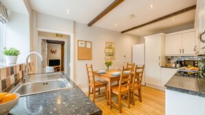 A modern kitchen with a central island, wooden dining table, and built-in cabinets. - 3 Bed in Seahouses (oc-cn103) (Seahouses)