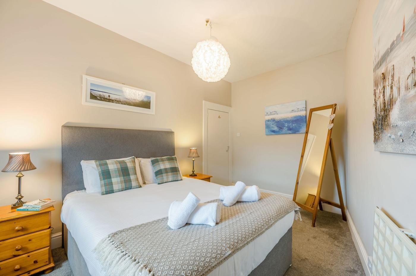A bedroom with a bed, bedside tables, a dresser, a mirror, and artwork on the walls.