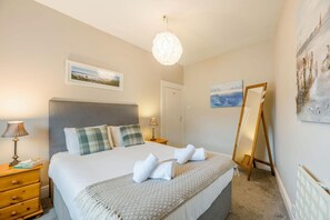 A bedroom with a bed, bedside tables, a dresser, a mirror, and artwork on the walls.