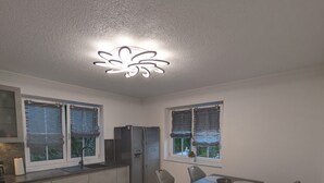 A modern kitchen with a dining area, featuring a central island, a refrigerator, and a ceiling light fixture. - Vacation rental, comfortable and modern, designed for discerning guests, near the main train station (Freudenstadt)