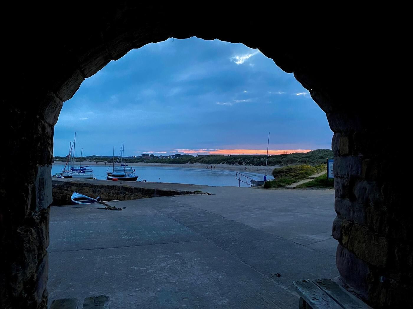 An archway leading to a harbor with boats and a calm sea.