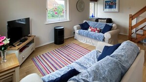 Ein Wohnzimmer mit Fernseher, einer Couch, einem Couchtisch, einem Teppich und einem Fenster mit Blumen.