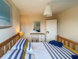 A hotel room with two beds, a desk, a mirror, a wardrobe, and a painting on the wall. - 2 Bed in Beadnell (oc-cn147) (Beadnell)