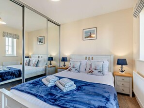 A hotel room with a large mirror, a bed with blue bedding, two bedside tables with lamps, and a picture on the wall.