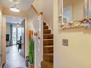 A staircase with a handrail, a wall-mounted decorative piece, and a door leading to a room with a television and a chair.