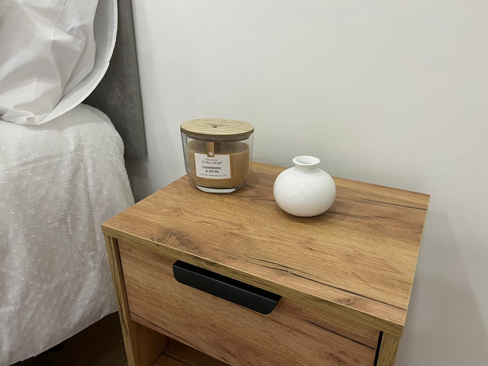 A wooden bedside table with a candle and a vase.