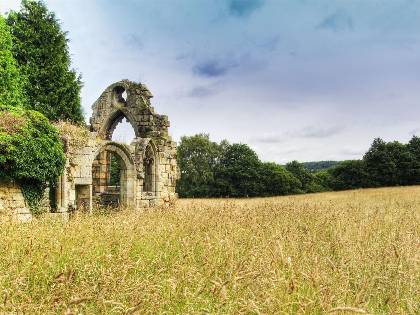 A historic stone structure with arches, surrounded by a field and trees.