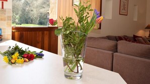 Ein Wohnzimmer mit Holzwand, einem Fenster mit Blick auf Bäume, einer Glasvase mit Blumen und einem Sofa.