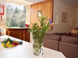 A living room with a wooden wall, a window with a view of trees, a glass vase with flowers, and a couch. - 2 Bed in Rowlands Gill (oc-cn192) (Rowlands Gill)