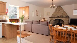 Eine Küche mit Steinofen, ein Essbereich mit Holzsesseln, eine Couch und ein Fernseher.