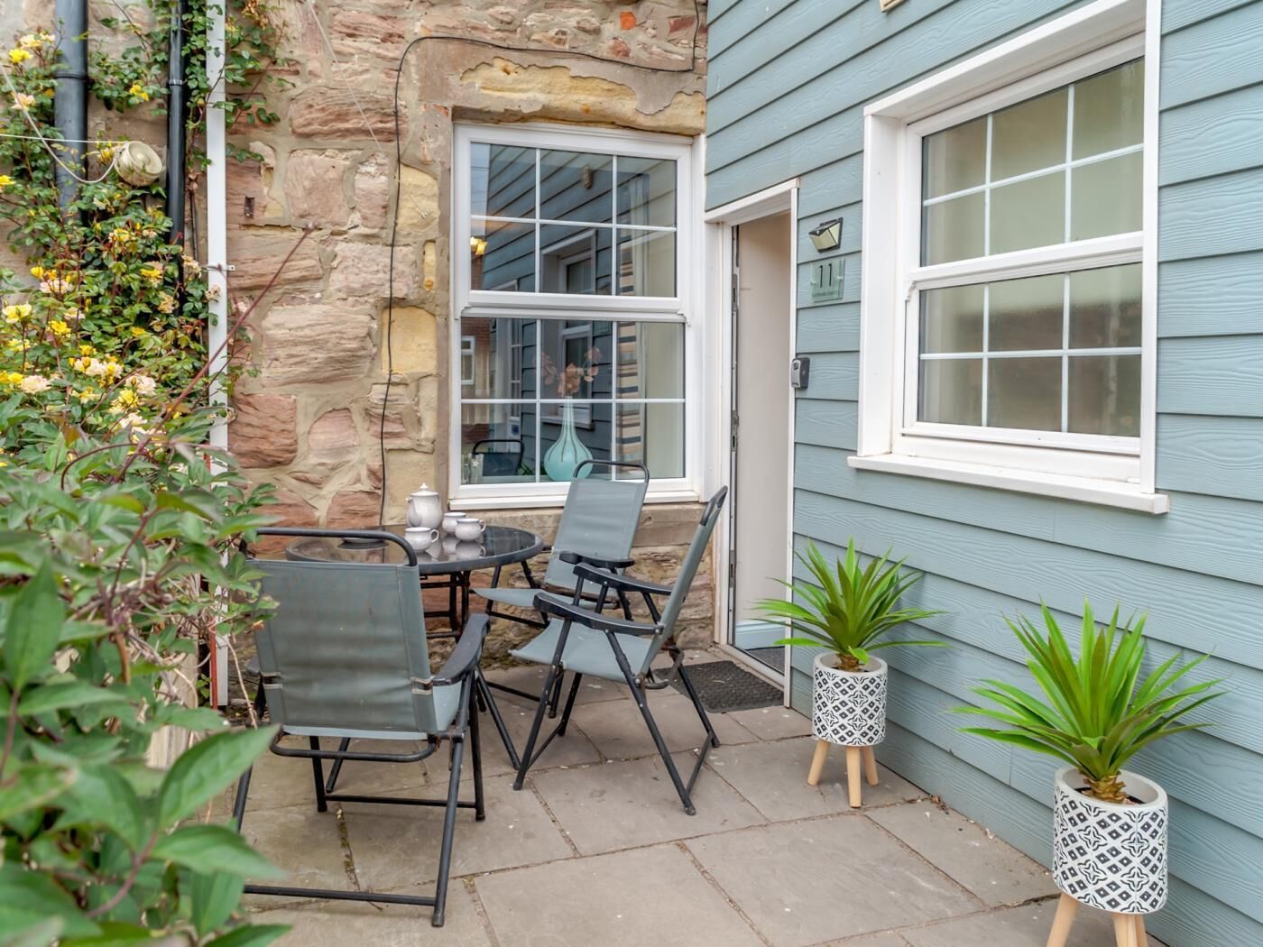 Une terrasse avec une table et des chaises, un pot de fleurs et un mur en pierre.