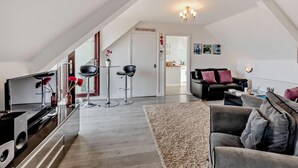 Een moderne woonkamer met een bank, salontafel en een televisie. Een trap leidt naar een keukenhoek.