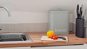 Een keuken met een spoelbak, een snijplank met groenten, een mes en een prullenbak.