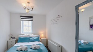 Een slaapkamer met een bed, een raam, een spiegel aan de muur, een bedlamp en een radiator.