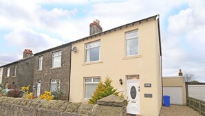 A two-story residential building with a stone wall in front, a door labeled 'Station Cottage,' and a garage door visible to the right. - 3 Bed in Seahouses (oc-cn182) (Seahouses)