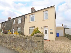 A two-story residential building with a stone wall in front, a door labeled 'Station Cottage,' and a garage door visible to the right. - 3 Bed in Seahouses (oc-cn182) (Seahouses)