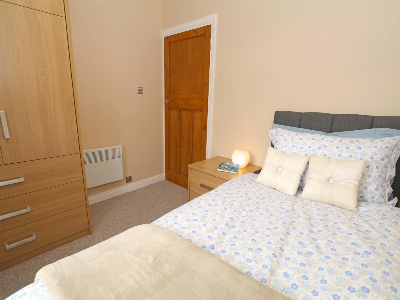 A bedroom with a bed, a wardrobe, a nightstand, and a door.