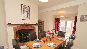 A dining room with a brick fireplace, a table set for four, and a view of the outside through a glass door. - 3 Bed in Seahouses (oc-cn182) (Seahouses)