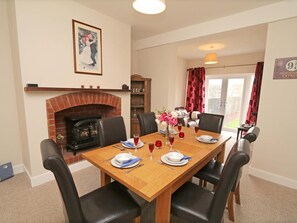 A dining room with a brick fireplace, a table set for four, and a view of the outside through a glass door. - 3 Bed in Seahouses (oc-cn182) (Seahouses)