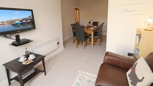 A living room with a television, a dining area with chairs and a table, a brown leather sofa, and a wall with a motivational quote. - 3 Bed in Seahouses (oc-cn182) (Seahouses)