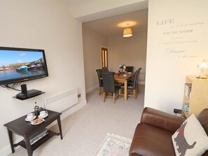 A living room with a television, a dining area with chairs and a table, a brown leather sofa, and a wall with a motivational quote. - 3 Bed in Seahouses (oc-cn182) (Seahouses)