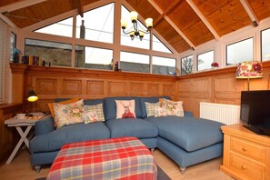 Ein gemütliches Zimmer mit einem blauen, modularen Sofa, einem karierten Hocker, einer Holz-TV-Kommode und einem Kronleuchter.