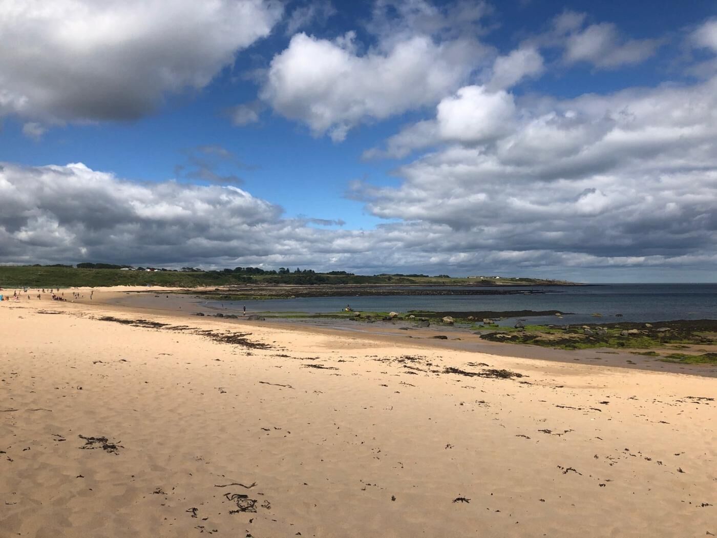 Ein Strand mit sandigem Ufer, ruhiger See und teils bewölktem Himmel.