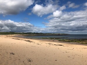 Ein Strand mit sandigem Ufer, ruhiger See und teils bewölktem Himmel.
