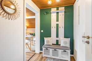 Ein Zimmer mit grüner Akzentwand, einer Sitzbank mit Stauraum, einem Spiegel und einer Tür mit modernem Griff.