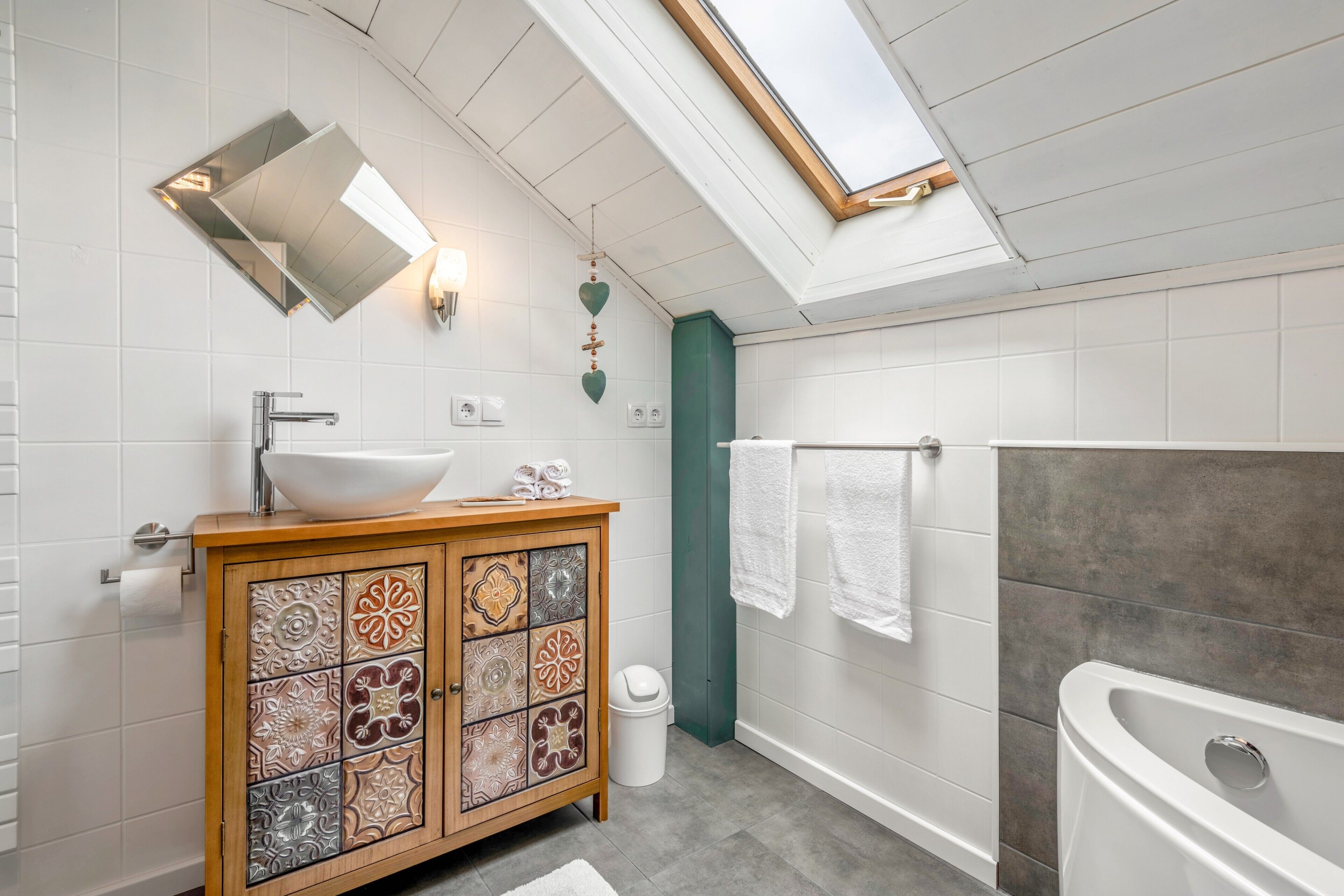 Ein modernes Badezimmer mit Oberlicht, einer freistehenden Badewanne und einem Waschtisch mit dekorativen Fliesen.