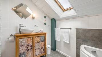 Ein modernes Badezimmer mit Oberlicht, einer freistehenden Badewanne und einem Waschtisch mit dekorativen Fliesen.