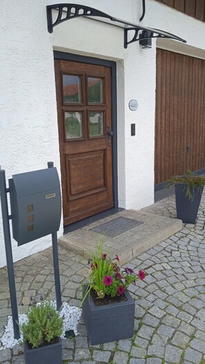 A building with a wooden door, a mailbox, and potted plants on a cobblestone path.