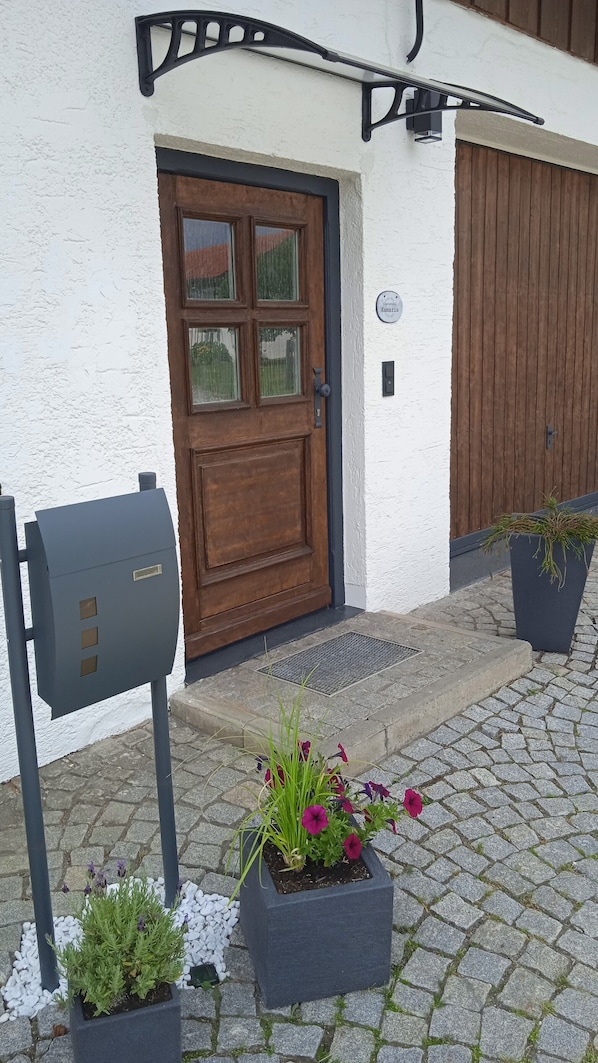 Un bâtiment avec une porte en bois, une boîte aux lettres et des plantes en pot, le tout situé sur un chemin pavé.
