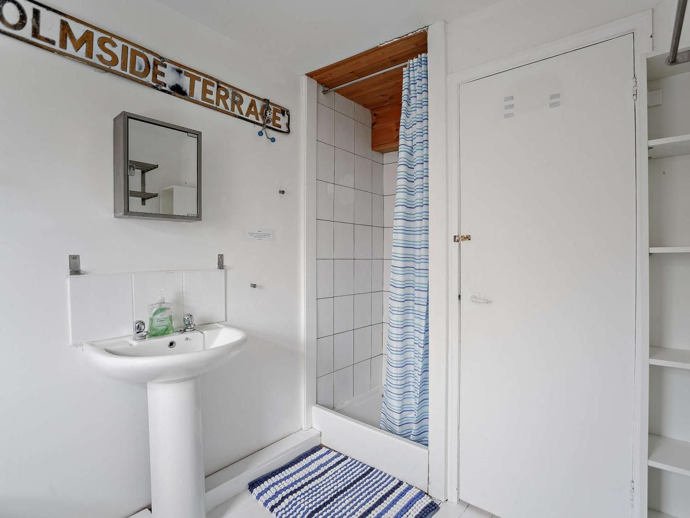 Un baño con un lavamanos blanco, un espejo, una ducha con cortina a rayas y una puerta con la etiqueta 'OLMSIDE TERRACE'.