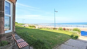 Een pand aan de kust met een gazon, een bankje en uitzicht op zee.
