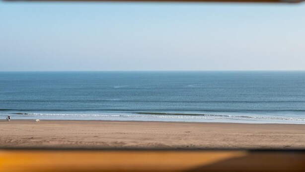 Een uitzicht op het strand, met heldere lucht, een rustige zee en een zandstrand.