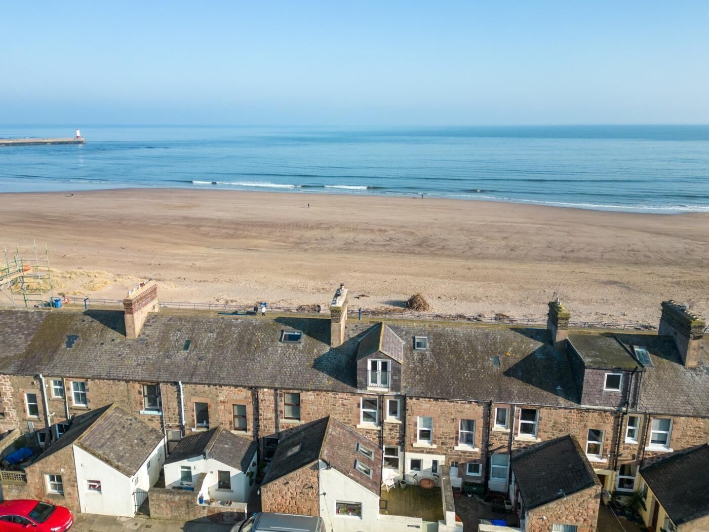 Une zone résidentielle côtière avec des maisons, une plage et un phare visible au loin.