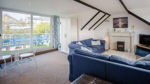 A living room with a blue sofa, a fireplace, a television, and a balcony with outdoor furniture. - 3 Bed in Low Newton By The Sea (oc-cn203) (Newton-by-the-Sea)