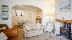 A cozy living room with a fireplace, a sofa, a dining table, and a chandelier. - 3 Bed in Low Newton By The Sea (oc-cn203) (Newton-by-the-Sea)