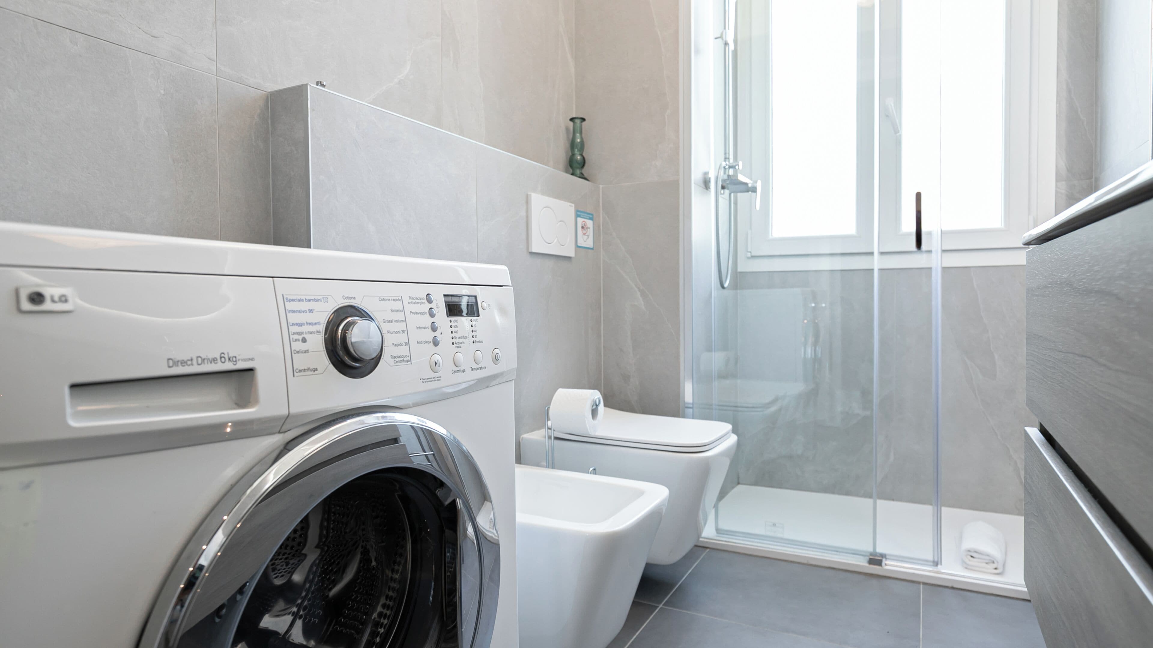 A modern bathroom with a Direct Drive 6kg washer, a toilet, and a glass shower enclosure.