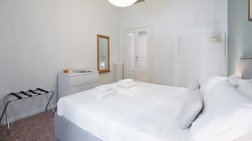 A hotel room with a bed, a bedside table, a radiator, a mirror, and a hanging light fixture.