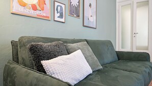 En grön soffa med två kuddar, en dörr och tre inramade tavlor på väggen.