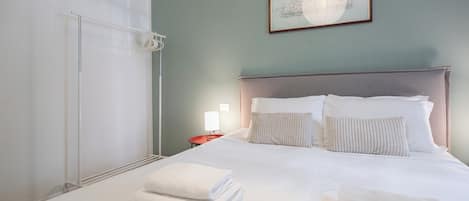 Une chambre d’hôtel avec un lit, des oreillers, une table de chevet avec une lampe et une serviette sur le sol.