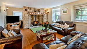 Ein Wohnzimmer mit Kamin aus Stein, Ledersofas, einem Couchtisch mit Büchern und einem Fernseher.