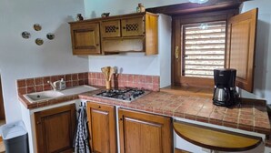 A kitchen with wooden cabinets, a gas stove, a sink, a coffee maker, and a window with blinds. - Charming Tuscan apartment with a pool, views, and a private terrace (Toscana)