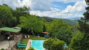 A swimming pool surrounded by lush greenery, a wooden deck, and a covered seating area. - Charming Tuscan apartment with a pool, views, and a private terrace (Toscana)